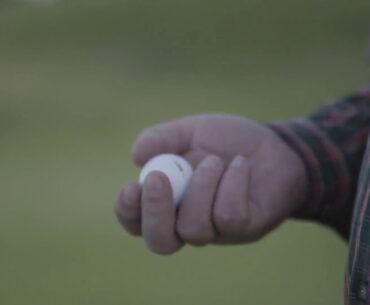 close up hand of mature man throwing up and catching golf ball standing on the golf fiel