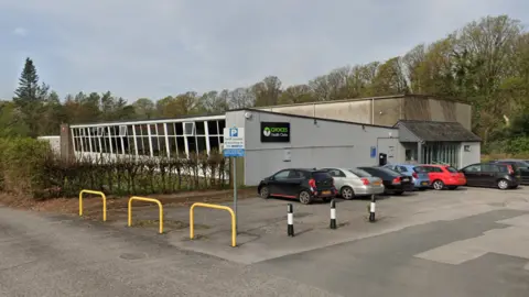 Google Choices Health Club from a side on view. The building design is single-storey concrete with panelled windows on the front face. There are a number of cars parked outside. 