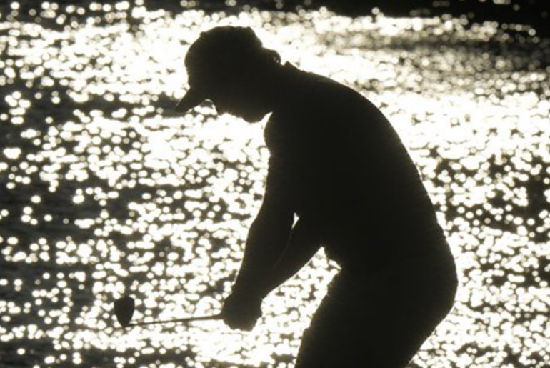 A Golfer starts their swing, silhouetted.