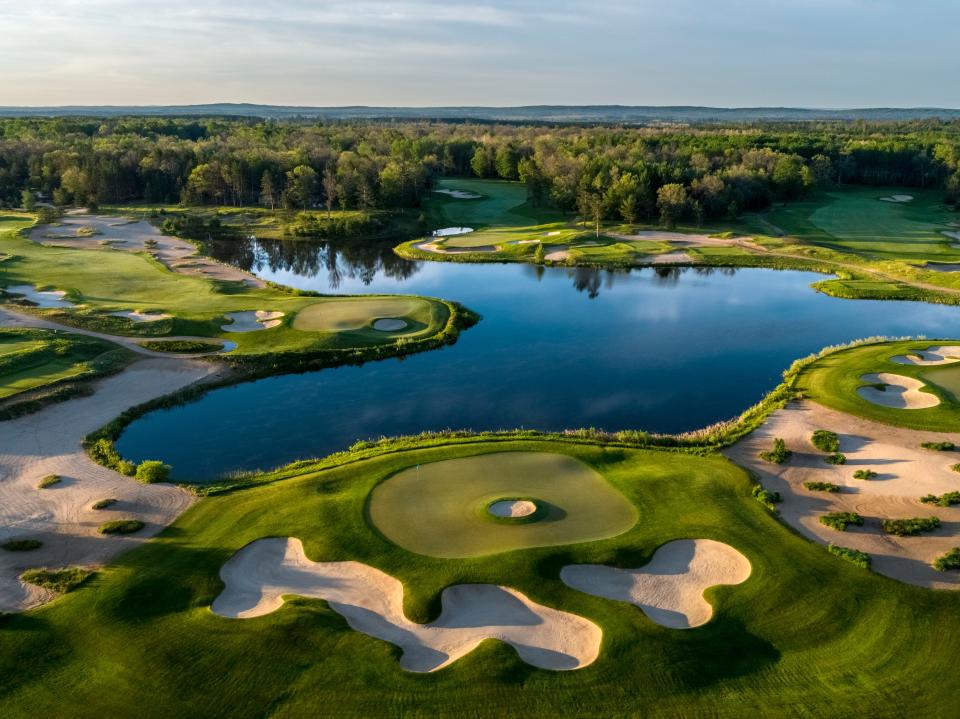 An overview of Forest Dunes Golf Club with a large irregularly shaped pond surrounded by golf-course greens. A forest is behind the course.