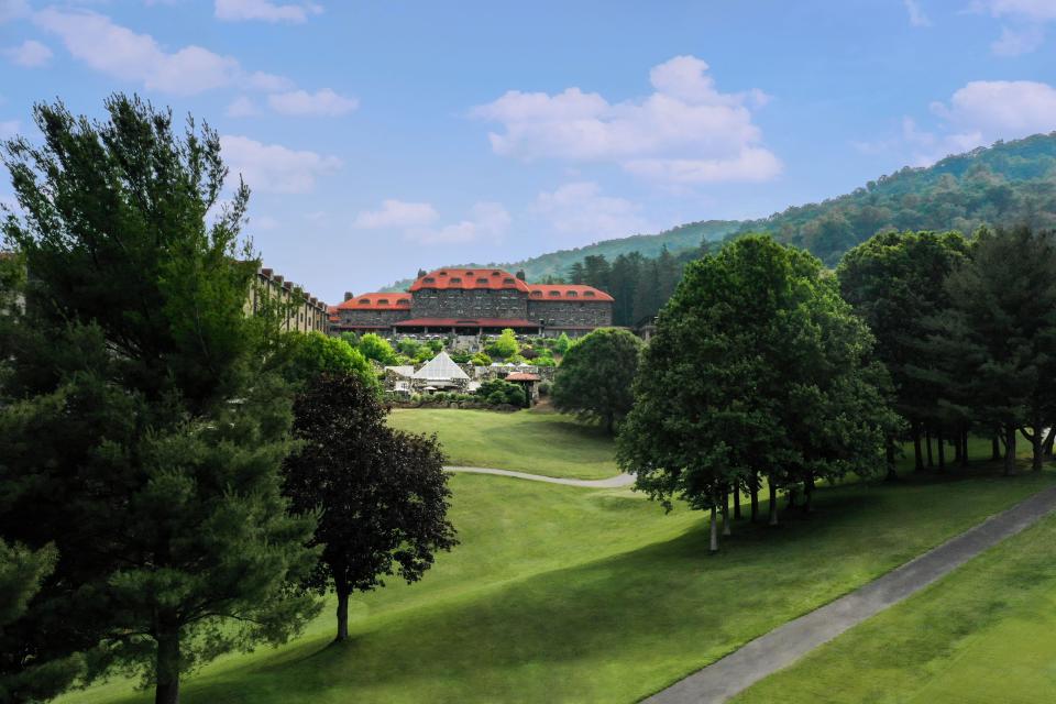 View of stone-covered building behind trees and greenery and in front of mountains at The Omni Grove Park Inn